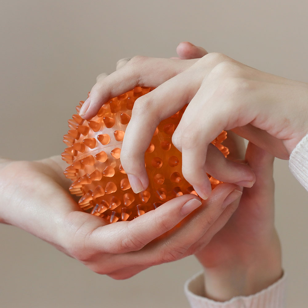 Three hands on an orange therapy ball